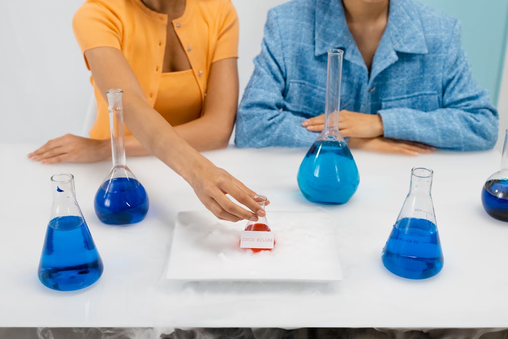 Two women in a laboratory setting conducting an experiment, using Erlenmeyer flasks containing blue liquid.